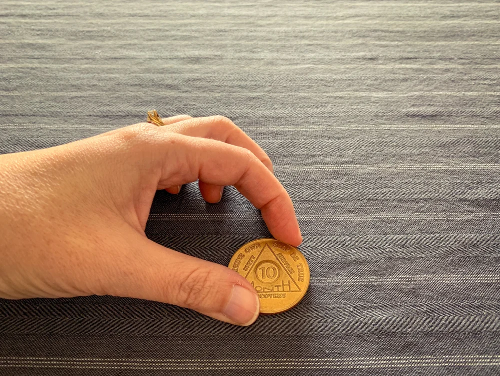 Someone places a 10-month Alcoholics Anonymous token on a table