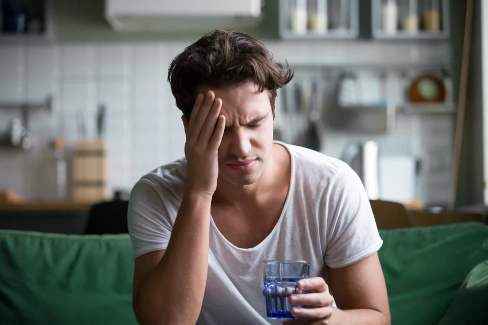 A man presses his hand to his forehead as he copes with a hangover