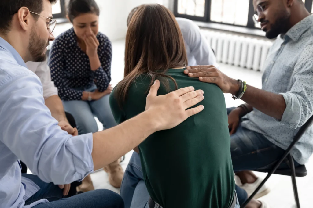 A couple of people comfort a woman at a rehab support group