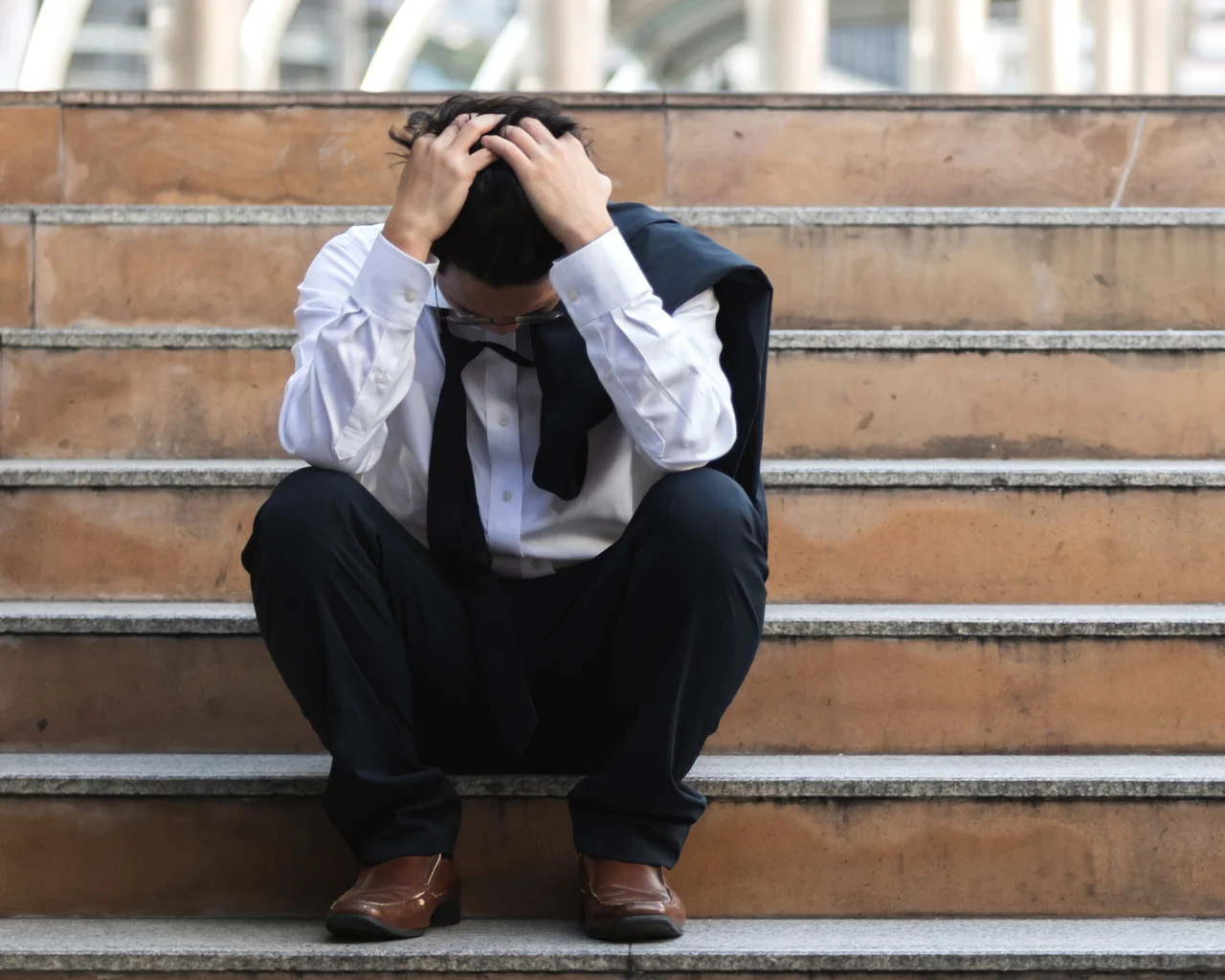 A distressed man in a suit grabs his hair while sitting on a staircase
