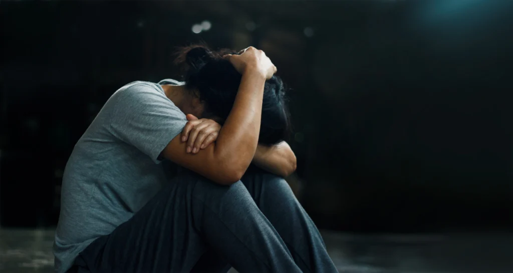 A depressed woman holds her head between her knees