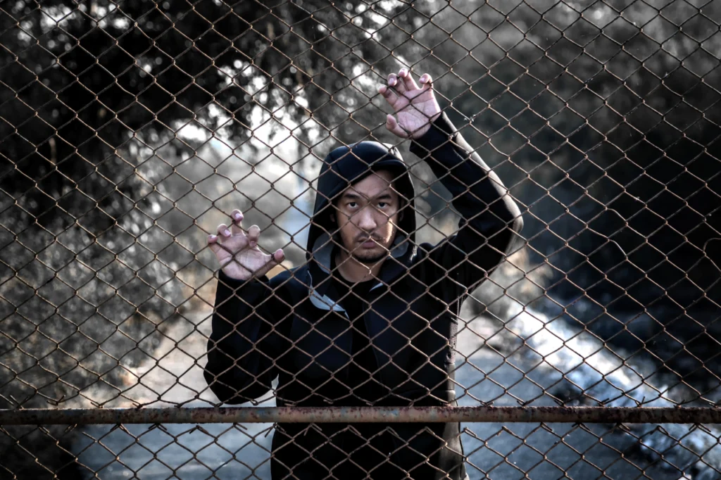 A depressed man grips a chain link fence