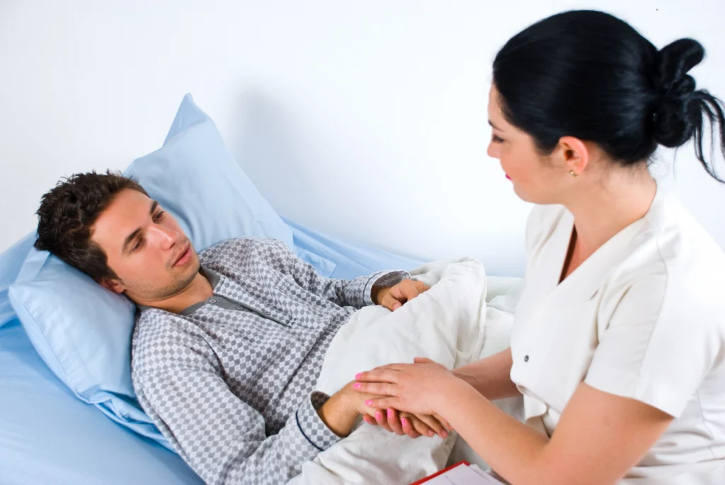A doctor reassures a patient in a hospital bed by holding his hand
