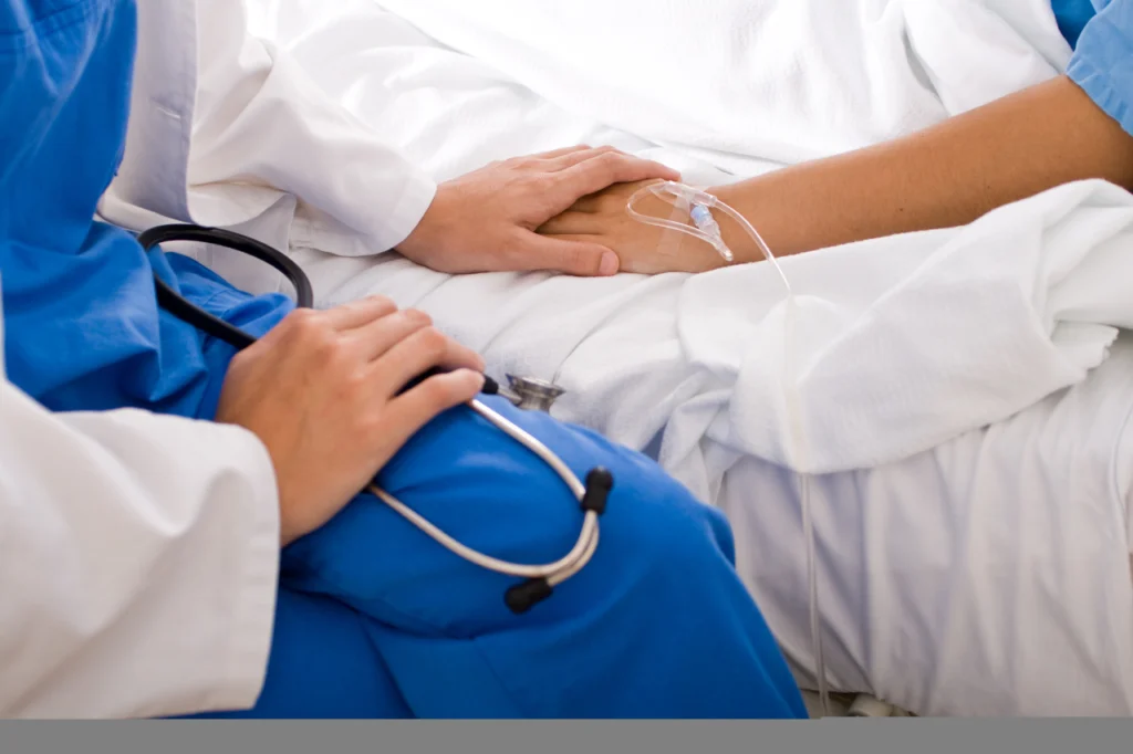 A doctor holds hands with a patient in a hospital bed