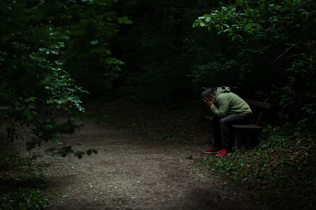 A depressed person sits alone in a dark park