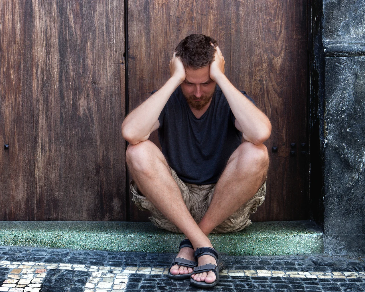 A depressed man grips the sides of his head while sitting on the ground