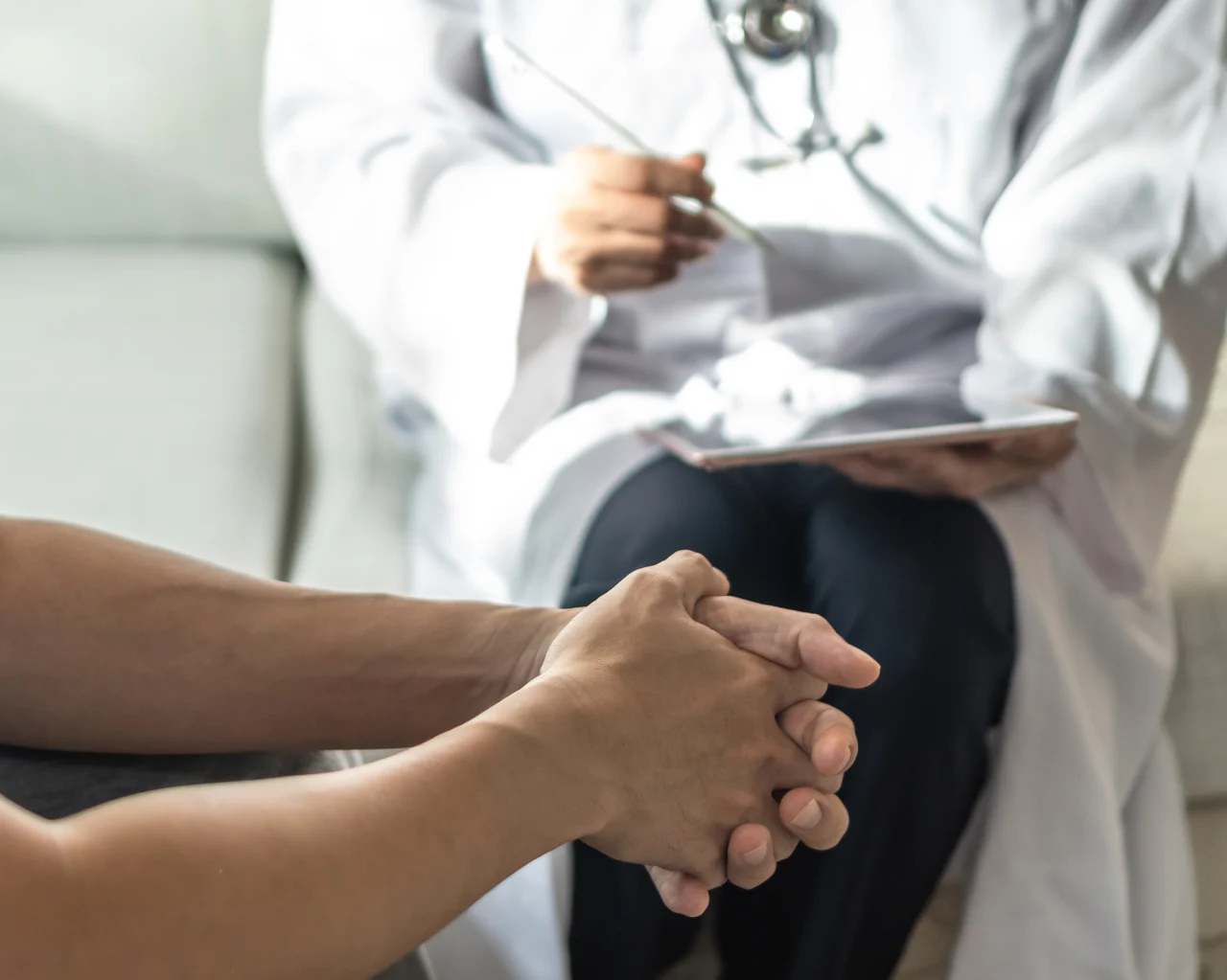 a patient holds their hands together as they speak with a doctor during a consultation