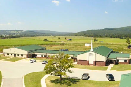 Aerial view of treatment center campus with cream-and-green-roofed buildings, parking area, landscaped grounds, and surrounding rural hills