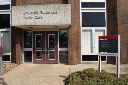 Exterior view of University Behavioral Health Care main entrance with brick facade, red entry doors, and facility signage on white panel