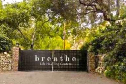 Exterior entrance gate with black fencing displaying Breathe Life Healing Centers signage surrounded by mature landscaping.