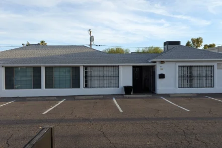 Exterior front view of white single-story treatment facility with barred windows, entrance door, and parking area