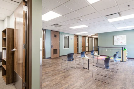 Interior group therapy space with blue chairs arranged around tables, artwork on walls, and natural lighting