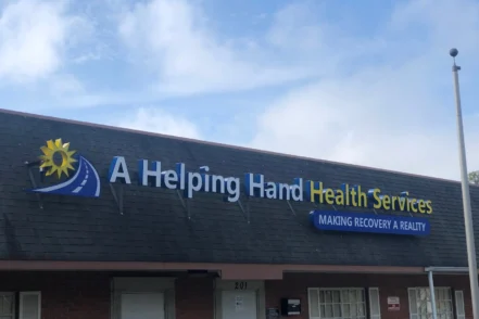 Exterior view of A Helping Hand Health Services building with illuminated sign, brick facade, entrance doors, and parking area