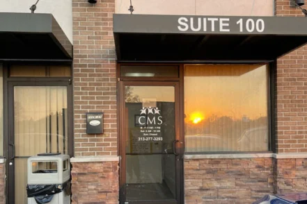 Exterior brick building with Suite 100 signage, glass entrance doors, and street-level parking visible.