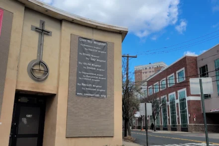 Exterior view of treatment center building with large cross, informational plaque, and street-facing entrance under clear sky.