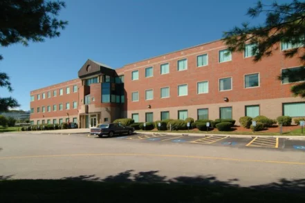 Exterior of red brick treatment center building with parking lot, landscaping, and multiple stories visible.