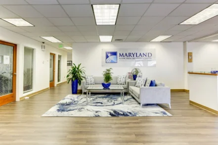 Interior reception area with contemporary furniture, light wood flooring, gray sectional seating, and facility branding
