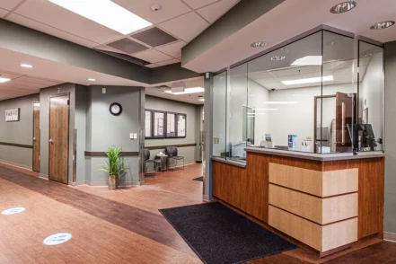 Interior reception lobby with wooden desk, glass partition window, and seating area with tile flooring