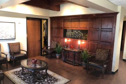 Interior reception lounge with dark wood paneling, comfortable seating, Desert Cove Recovery signage, and warm ambient lighting